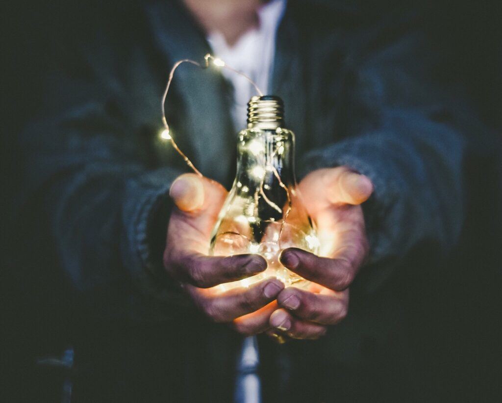 Hands holding a lit light bulb, representing custom-fit ideas and innovation